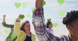 Multiple green hearts floating against group of diverse people protesting at the beach
