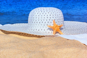 Wall Mural - Close-up view of a sun hat on a sandy beach by the sea, selective focus. Beach holiday concept, background with copy space for text