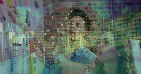 Canvas Print - Spinning globe against diverse male and female colleagues discussing over whiteboard at office