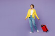 Traveler fun woman wear yellow casual clothes hold suitcase bag look aside isolated on plain purple background. Tourist travel abroad in free spare time rest getaway. Air flight trip journey concept.