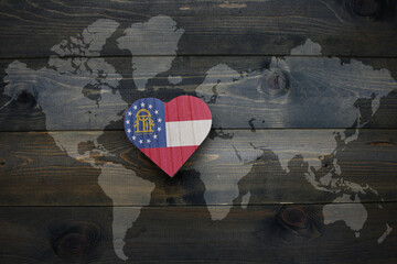 Wall Mural - wooden heart with national flag of georgia state near world map on the wooden background.