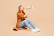 Full body young woman she wear orange shirt casual clothes sits on pennyboard skateboard scream in megaphone about hot news isolated on plain pastel light beige background studio. Lifestyle concept.