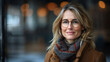 © amixstudio - Portrait of a smiling middle-aged Caucasian woman wearing glasses, a scarf, and a coat, with a blurred city background and warm lights.