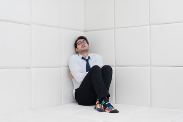 Sad and frustrated businessman in formal wear sitting in a white room in a mental hospital	