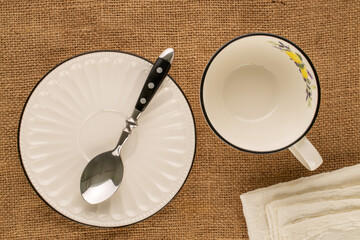 Wall Mural - One white porcelain cup with saucer, spoon and napkin on jute cloth, macro, top view.