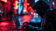Hooded figure using laptop on city street at night with neon lights. Cyber security and digital privacy concept with copy space. 