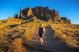 Fototapeta Zwierzęta - Hiker in a straw hat walking towards rock formations named Superstition Mountains in Lost Dutchman State Park, Arizona.