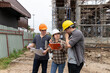 © skarie - Team of construction workers discussing project details with blueprint in construction site.