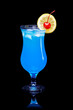 Blue Lagoon cocktail garnished with lemon slice and cherry served in a classic hurricane glass isolated on black reflective surface and dark background.