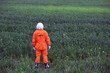 Rear view of man wearing orange astronaut space suit and space helmet standing in green grass outdoors. Travel concept