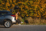 Fototapeta Na drzwi - a smiling woman sits in the trunk of a car on the background of an autumn forest