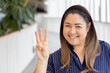 Happy smiling middle aged asian woman pointing up 3 fingers, three points, number three, third point