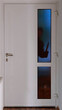 Ein Einbrecher steht in der Dunkelheit mit einem Messer vor einer Eingangstüre und schaut durch die Glasscheibe in die Wohnung oder Haus rein

