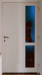 Ein Einbrecher steht in der Dunkelheit mit Einbruchs Werkzeug vor einer Eingangstüre und schaut durch die Glasscheibe in die Wohnung oder Haus rein

