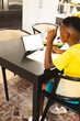 African American boy sitting at table, doing homework and looking at tablet at home with copy space