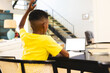 African American boy sitting at table, raising hand near tablet at home with copy space