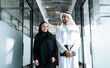Man and woman with traditional clothes working in a business office of Dubai. Portraits of  successful entrepreneurs businessman and businesswoman in formal emirates outfits walking down the office.