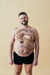 Man posing for a male edition body positive beauty set. Shirtless guy wearing boxers underwear  with writings drawn on his body.