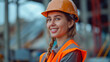 Portrait of a young woman in a protective helmet against a production background. She is a factory worker or a construction engineer.