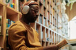 © Clique Images - Serious guy in headphones and eyeglasses looking through text in open book while sitting against stacks of bookshelves