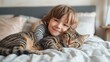 A little girl tenderly hugs her kitten and lies on the bed in the morning in a bright bedroom. Friendship concept between child and pet, copy space for text
