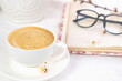 A cup of fresh morning cappuccino notepad and glasses on the table. Morning relaxation. Spring mood. Selective focus.