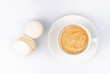 Cup of cappuccino and two macarons on white background. Top view. Close-up.