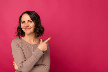 Studio portrait of a mature smiling woman pointing aside over pink backdrop.