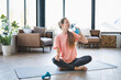 Young fit woman in sporty clothes drinking water during training at home. Female athlete hydrating while doing yoga stretching on fitness mat in the living room