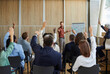 © Studio Romantic - Young colleagues raising hands to ask questions during business meeting in office. Diverse business people voting at the conference in meeting room listening their young male speaker.