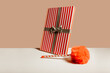 © ADDICTIVE STOCK - Striped gift box with ribbon and pom-pom on beige background