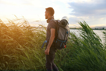 Wall Mural - A man is walking through a field with a backpack on. Scene is peaceful and serene, as the man is surrounded by nature