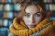 Intimate portrait of a woman with freckles wrapped in a yellow knit scarf, with bookshelves in the background