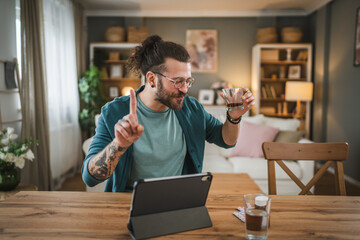 One adult man with eyeglasses drink alcohol and listen music on tablet home