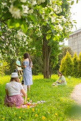 Three female artists painting on plein air in spring park. Women art process in botanical floral garden with blooming trees. Girls in summer dresses drawing view from the back