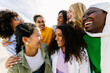 © Xavier Lorenzo - Seven happy young adult women from different cultures laughing together outdoors. Female friendship concept with diverse group of girls friends hugging each other having fun at city street