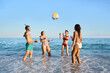 © CarlosBarquero - A group of cheerful young friends in swimwear enjoying leisure time on the shore on the sea, playing with a beach ball under the blue sky. Gen z people having fun in summer vacations