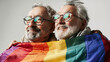 Inclusion & diversity at pride. Senior gay male couple hugging at pride month celebration with rainbow flag & glasses. Elderly smiling homosexuals at LGBTQ+ parade. White background