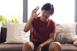 Asian teenage boy sitting on couch at home, making hand gesture during a video call
