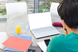 Fototapeta  - School work occupies teenage Asian boy, sitting at a table outside at home with a laptop, copy space