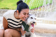 Cheerful young woman in a casual outfit cuddling with her adorable schnauzer beside a water fountain