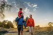Family on a nature walk, with a child on father's shoulders, enjoying a serene sunset in the countryside, symbolizing family bonding and outdoor enjoyment.