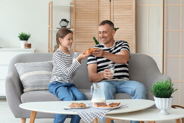 Poster - Little girl with her father sitting on sofa, drinking milk and eating pastries in living room