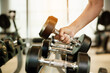 Close up hand holding dumbbell on floor in gym with woman background. Object goal weightlifting bodybuilding.