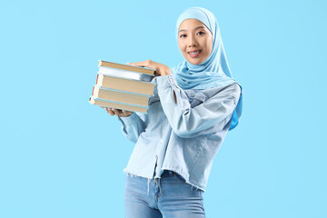 Sticker - Beautiful young Asian woman in hijab with books on blue background