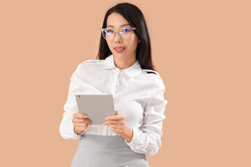 Wall Mural - Young Asian businesswoman in eyeglasses using tablet computer on beige background