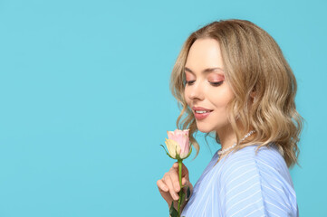 Wall Mural - Young woman with beautiful rose on blue background