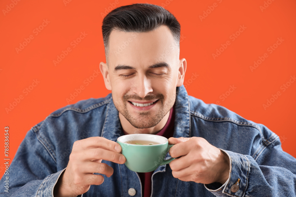 Handsome man with cup of tea on orange background, closeup
