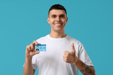 Sticker - Young happy man holding driver license and showing thumb-up on blue background