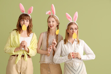 Sticker - Young girls with Easter bunny ears and paper eggs on color background